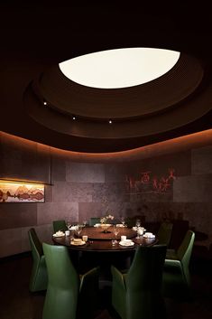 a round dining room with green chairs and a wooden table in the center is illuminated by a circular light