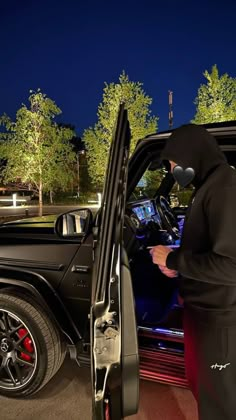 a man in a black hoodie standing next to a car with the door open