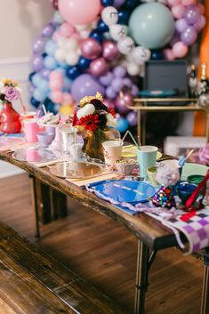 the table is set up for a party with balloons in the background and decorations on it