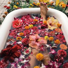 a person's feet in a tub filled with water surrounded by flowers and petals