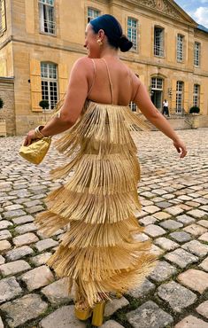 a woman in a gold dress is walking on the cobblestone street with her back to the camera