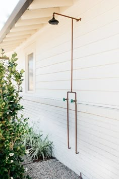 an outdoor shower head on the side of a white house with plants in front of it