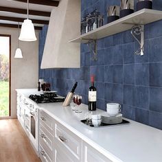 a kitchen with white cabinets and blue tiles on the backsplash, wine bottles are sitting on the counter