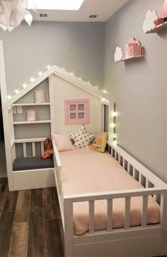 a white bed with a pink pillow and some lights on the headboard is in a gray room