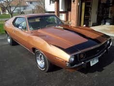 an orange muscle car parked in front of a brick building