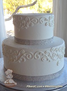 a three tiered white wedding cake on a silver platter in front of a window