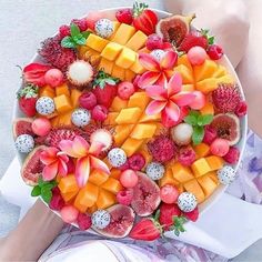 a platter filled with fruit and flowers on top of a white plate next to a woman's legs