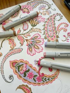 three pens are sitting on top of a piece of paper that has paisley designs on it