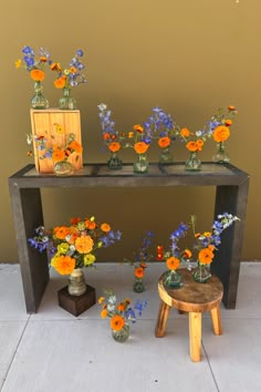 several vases with flowers sitting on top of a wooden table next to a stool