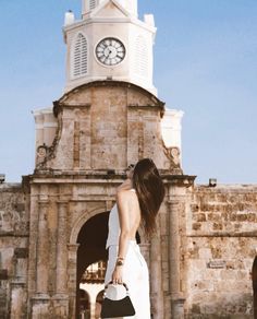 a woman is standing in front of an old building with a clock tower on top