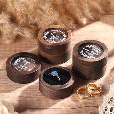 three wooden boxes with wedding rings inside on a table next to dried flowers and feathers