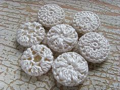 four crocheted white buttons sitting on top of a lace covered table cloth,