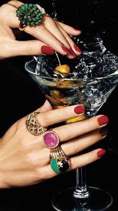 two hands with rings on their fingers are next to a martini glass filled with liquid