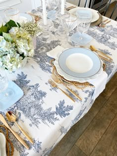 a table set with blue and white plates, silverware and flowers in vases