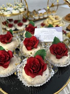 some cupcakes with white frosting and red roses on them sitting on a table