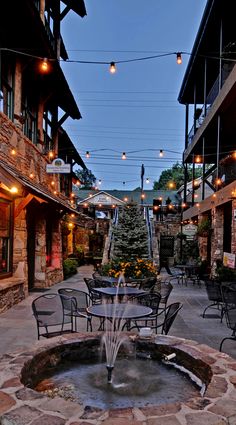 an outdoor patio area with tables and chairs, lights strung from the building to the street