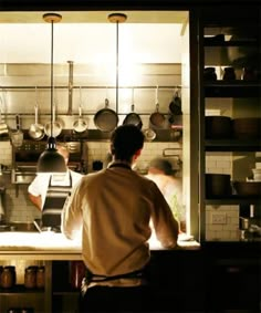 two men working in a kitchen with pots and pans hanging on the wall behind them