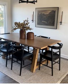 a dining room table with black chairs and a plant in a vase on top of it