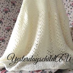 a white crocheted blanket sitting on top of a floral print bed coverlet