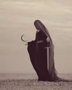 a woman dressed in black is standing on the beach and holding a crescent shaped object