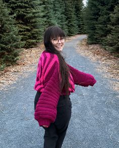 a woman standing in the middle of a road with her arms spread out and trees behind her