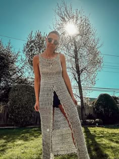 a woman standing in the grass wearing a long crochet dress and sun glasses