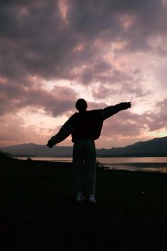 a man standing on top of a lush green field next to a lake under a cloudy sky