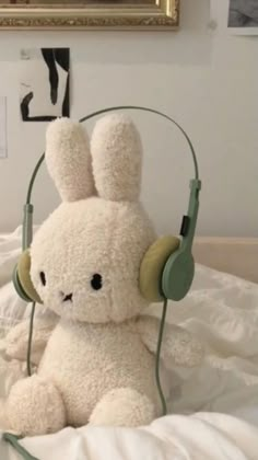 a white stuffed animal with headphones on top of a bed next to a painting