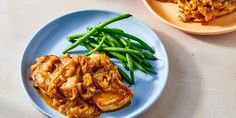 a blue plate topped with green beans next to another plate filled with meat and vegetables