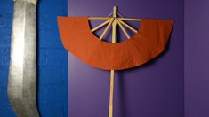 a purple wall with an orange and red paper fan on it next to a silver knife