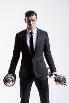 a man in a suit and tie holding two silver gloves with one hand on his hip