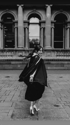 black and white photograph of woman in cape walking on sidewalk near large building with columns