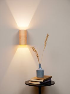 a small table with a vase on it next to a wall light that is turned on