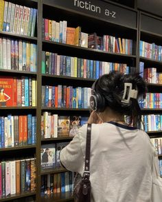 a woman wearing headphones standing in front of a book shelf with books on it