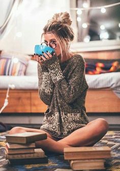 a woman is sitting on the floor drinking from a blue mug while looking at books