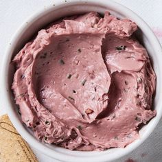 a white bowl filled with pink frosting next to a cracker