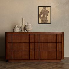 a wooden dresser with vases on top of it in front of a framed nude image