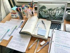 an open laptop computer sitting on top of a wooden desk next to lots of writing