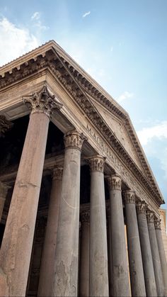 an old building with many columns on the front and side, under a cloudy blue sky