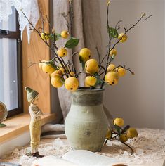 a vase filled with lemons sitting on top of a table next to a window