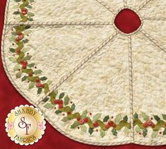 a quilted christmas table topper with holly and berries on the edge, sitting on a red background