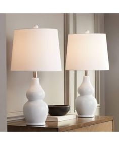 two white vases sitting on top of a wooden table next to a light fixture