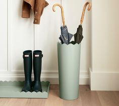 two rain boots and umbrellas sitting in a green container next to a coat rack