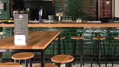 a bar with wooden stools and green tiled walls in the back ground, surrounded by black tile