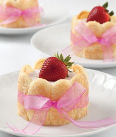 four small desserts on white plates with pink ribbons and strawberries in the middle