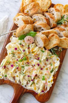 a wooden platter filled with food on top of a white marble countertop next to bread