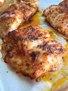 four pieces of chicken sitting on top of a white paper covered in mustard and seasoning