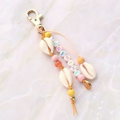 a key chain with seashells and letters on it sitting on a white surface