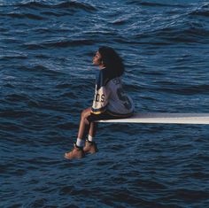 a woman sitting on the edge of a boat in the ocean looking up at the sky