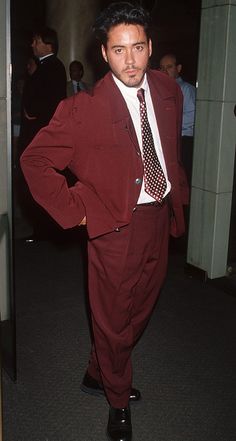 a man in a red suit and tie standing with his hands on his hips while looking at the camera